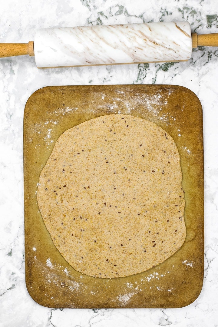 Whole grain pizza dough on pizza stone on white marble with white marble rolling pin.