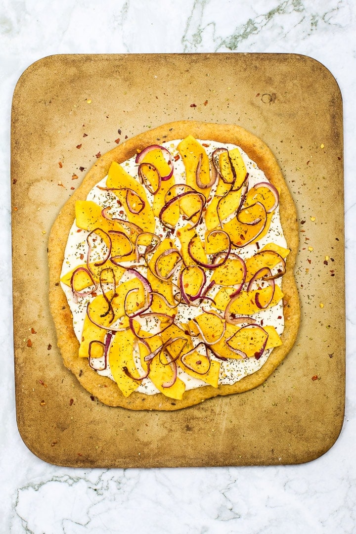 Roasted squash white pizza on pizza stone on white marble.