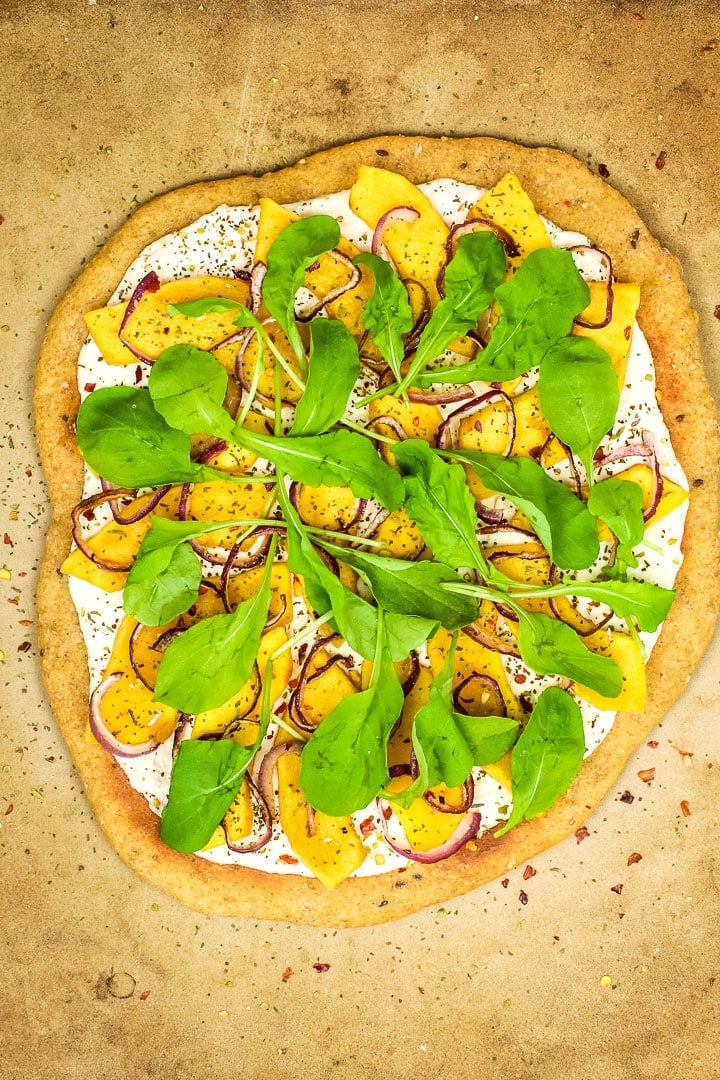 Roasted squash white pizza on pizza stone with arugula