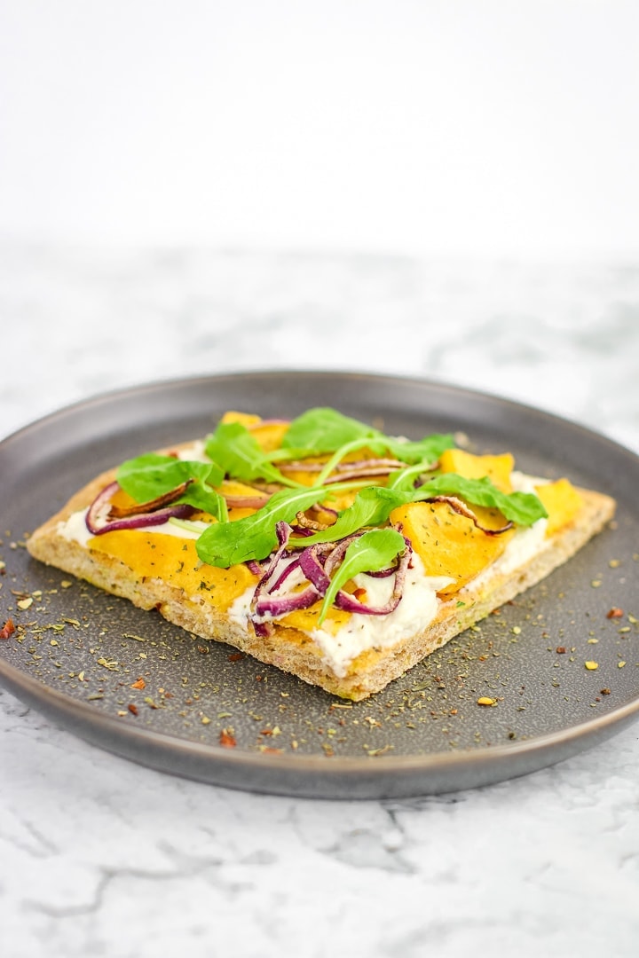 roasted squash white pizza topped with arugula on a gray plate on marble.