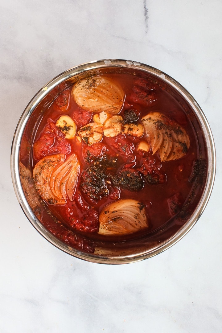 Instant Pot pot with cooked ingredients: tomatoes, quartered onion, smashed garlic cloves and Italian seasonings.
