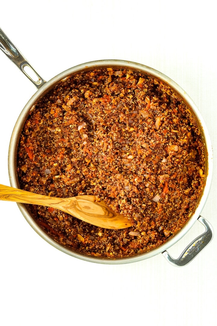 stainless steel skillet with cooked quinoa taco meat and wooden spoon.