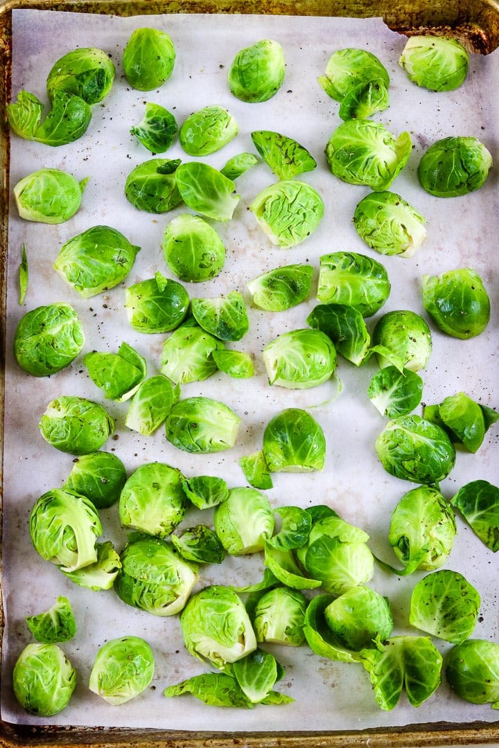 Parchment paper lined baking sheet with raw brussels sprouts halves. 