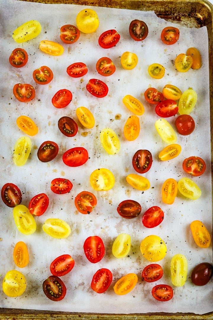 Parchment paper lined baking sheet with raw cherry tomato halves. 