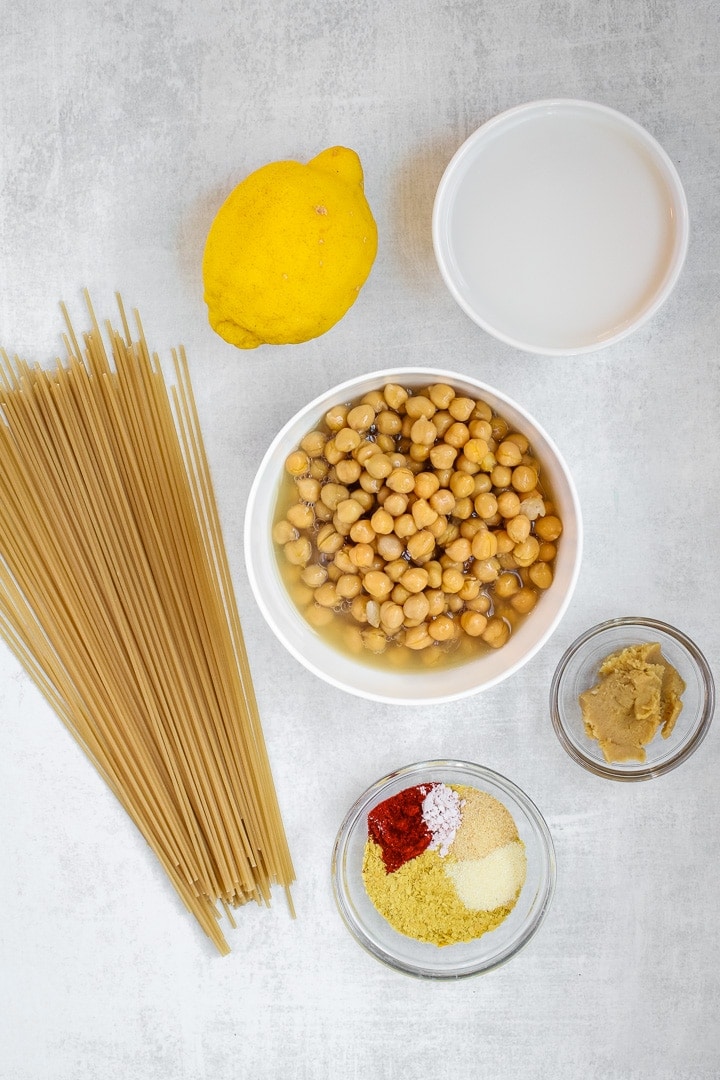 Dry brown rice spaghetti, lemon, chickpeas, plant milk, miso paste and spices on a gray background.