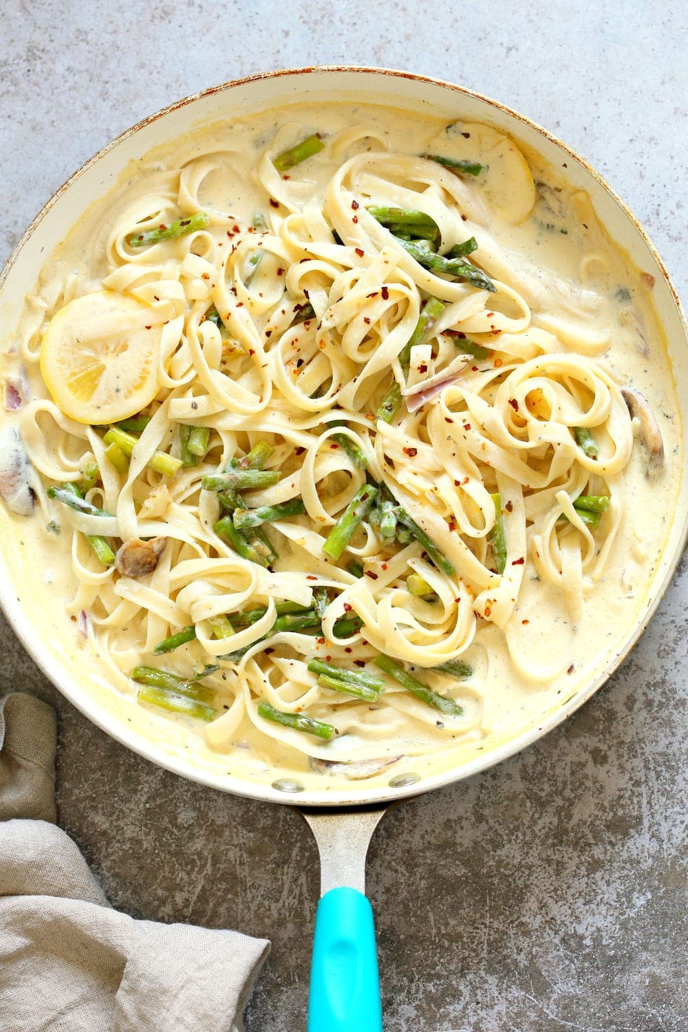 Skillet of creamy lemon pasta with asparagus, lemon slices and red pepper flakes.