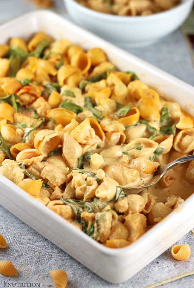 Small pasta shells with buffalo cheese sauce and herbs in a white rectangular baking dish with fork.