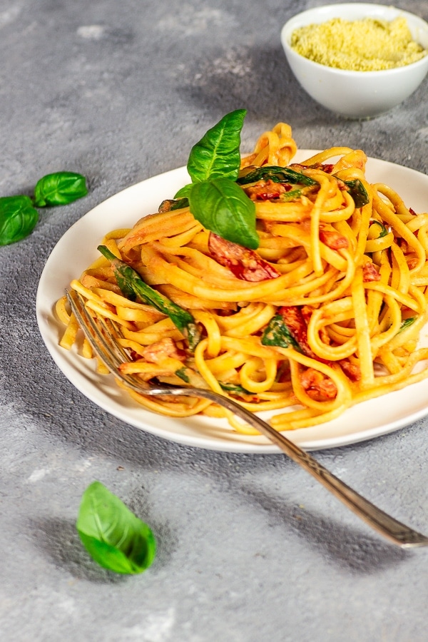 White plate with linguine with tomato alfredo sauce, with basil leaves, fork and vegan Warm in a white bowl.