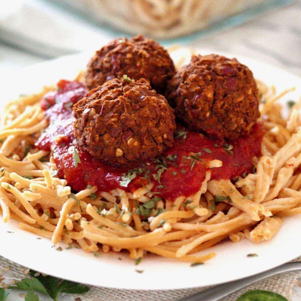 white plate with spaghetti and vegan meatballs, topped with herbs.