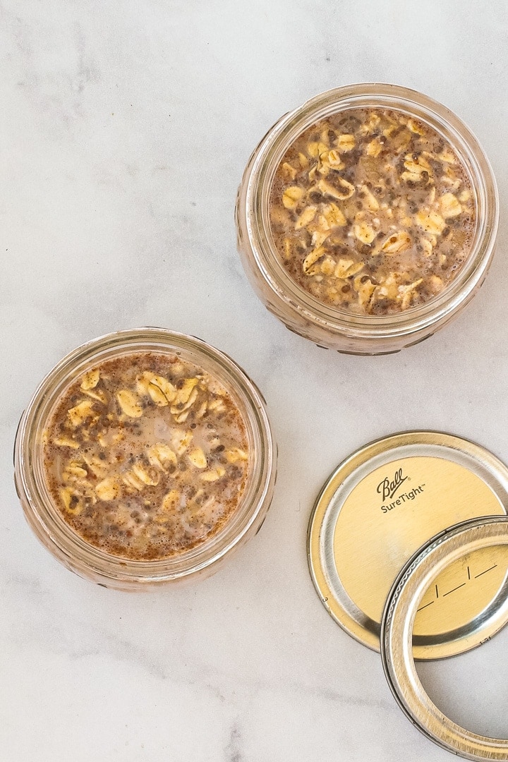 Banana overnight oats in small mason jars with no toppings, with a lid on gray marble.