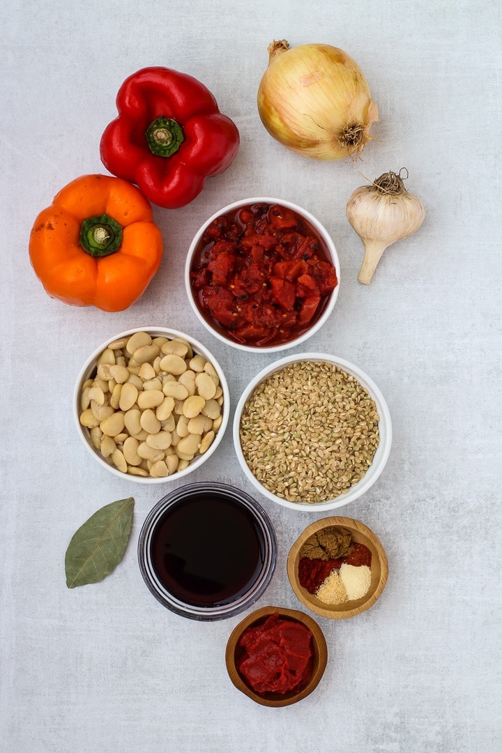 Red and orange bell peppers, yellow onion, garlic bulb, bay leaf, white dishes of butter beans, diced tomatoes, brown rice, and spices, red wine and tomato paste.