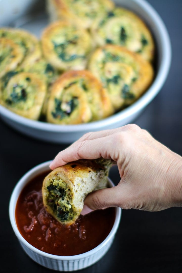 Spinach & Cheese Pizza Rolls in round baking pan and one being dipped in marinara sauce