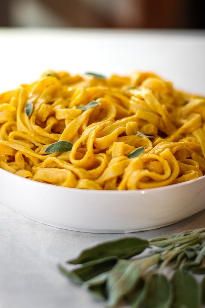 Vegan pumpkin pasta sauce with fresh sage over fettuccine in a white bowl.