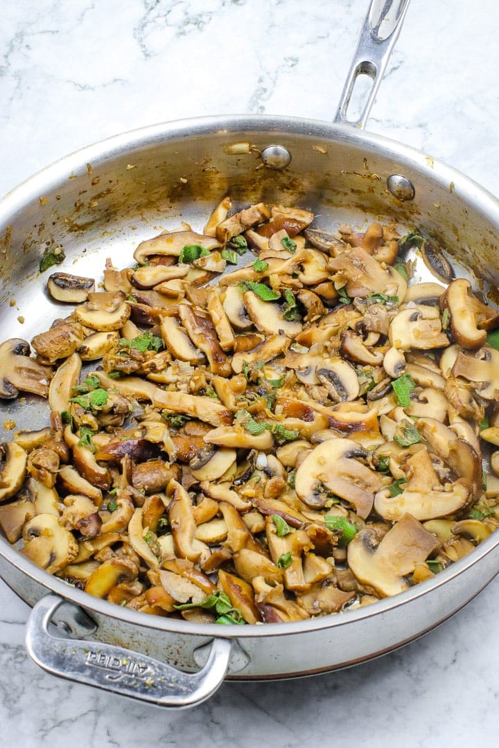 gesauteerde sjalotten, champignons en salie in een koekenpan op grijs marmer.