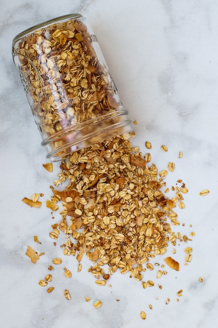 Mason jar of granola spilling out onto white marble.