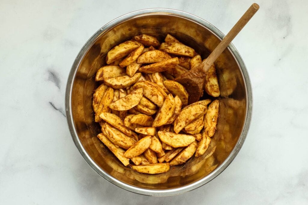 Tossing apple slices, cinnamon and date paste in a mixing bowl with a wooden spoon.