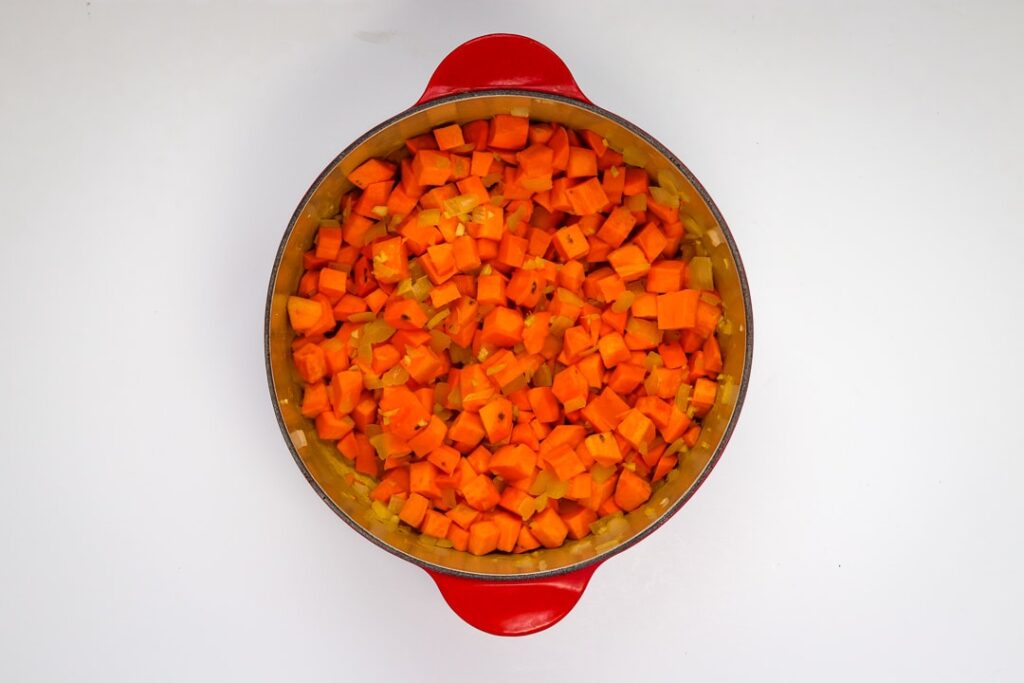 Sweet potatoes and aromatics simmering in a red dutch oven.