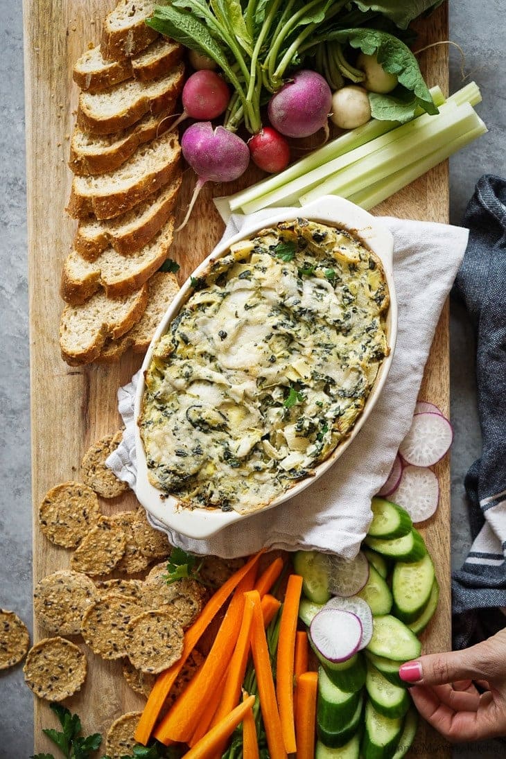Spinach Artichoke Dip in a white bowl with crackers, bread and veggies