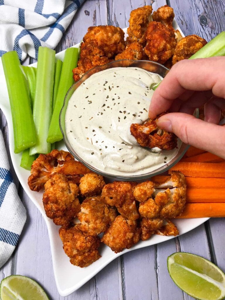 Cauliflower Buffalo Wings hand dipping into ranch dressing