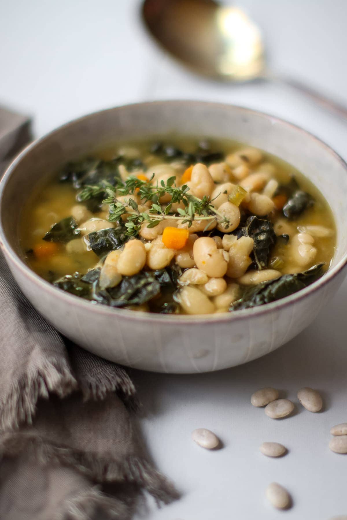 White bean soup with kale in a pale blue bowl with fresh thyme.