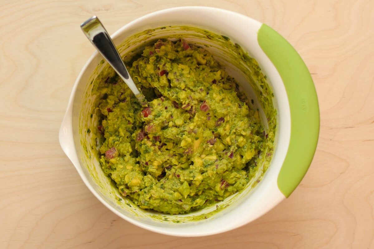 Mixing bowl with large spoon and finished guacamole. 