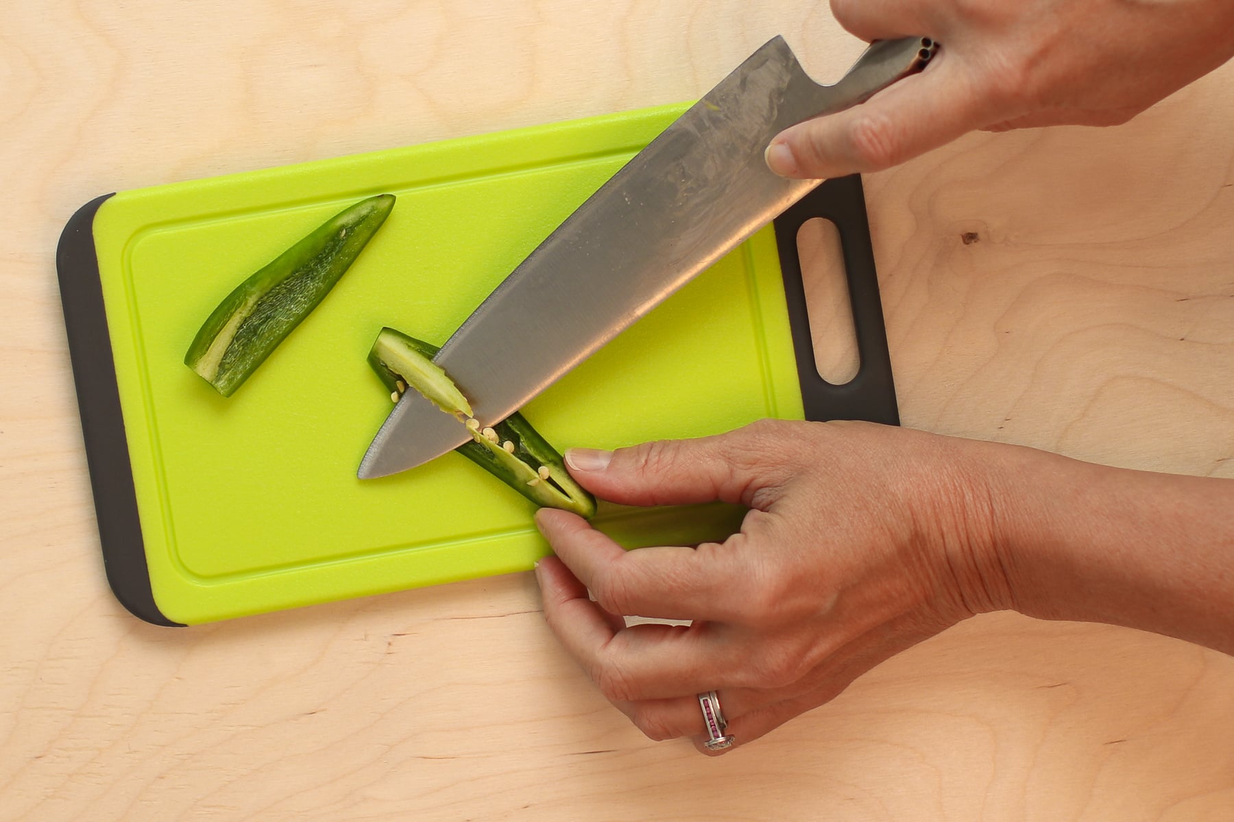 I'm using a chef's knife to cutting a jalepeño on a green cutting board.