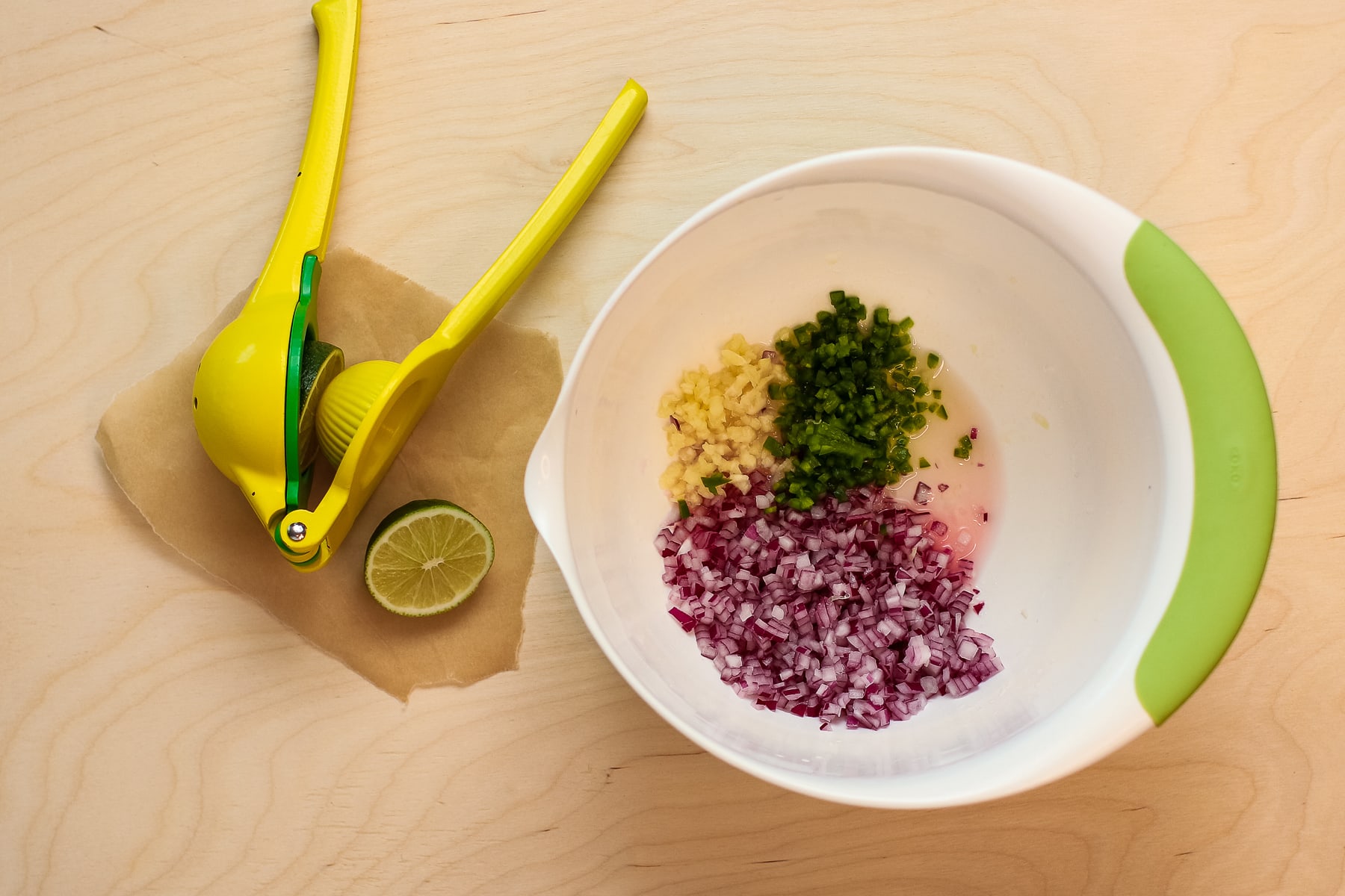Ingredients in a white mixing bowl, with yellow lime squeezer and lime next to it on a brown board. 