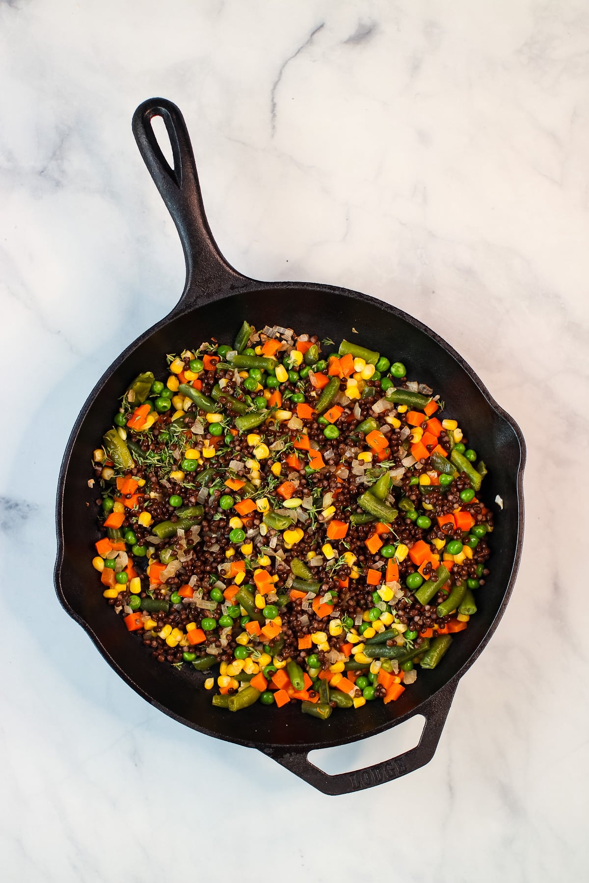 Mixed vegetables, lentils and thyme in a cast iron skillet.