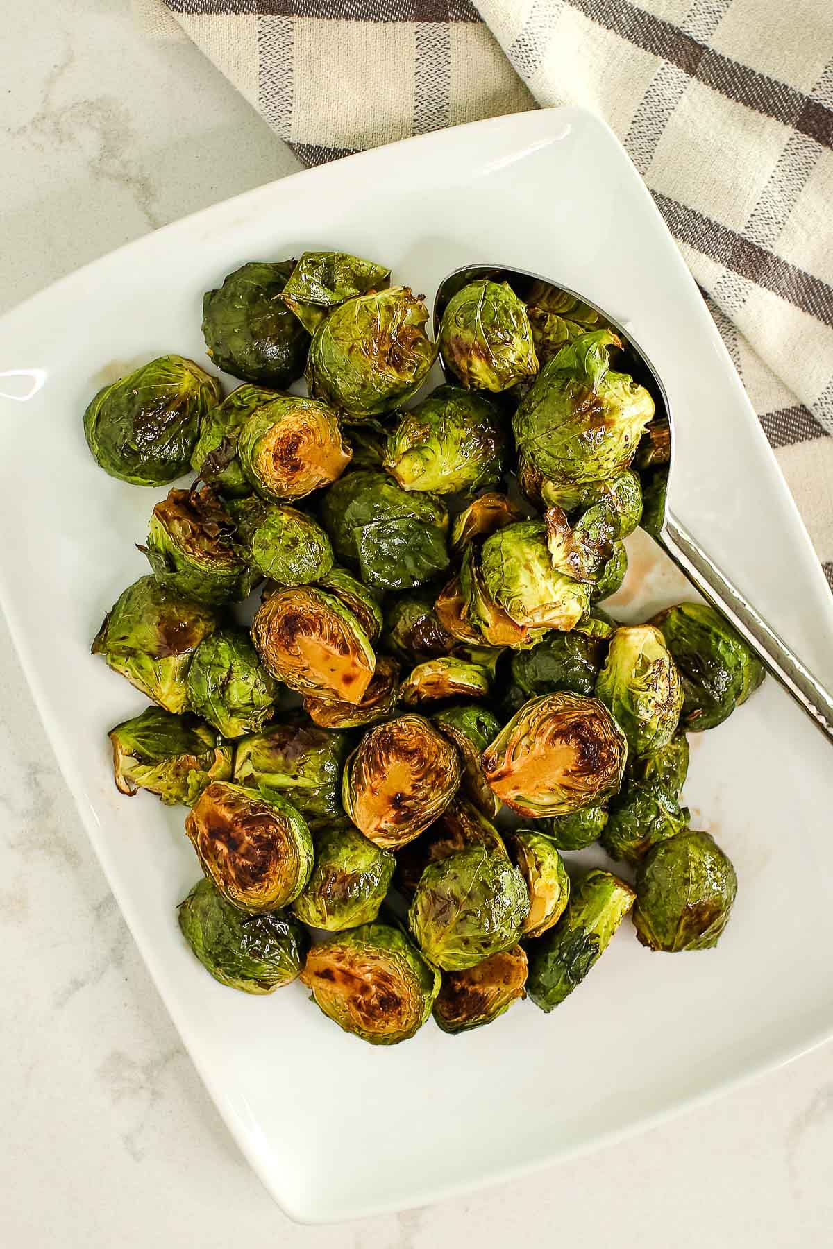 Plate of finished glazed Brussels sprouts with spoon and towel.