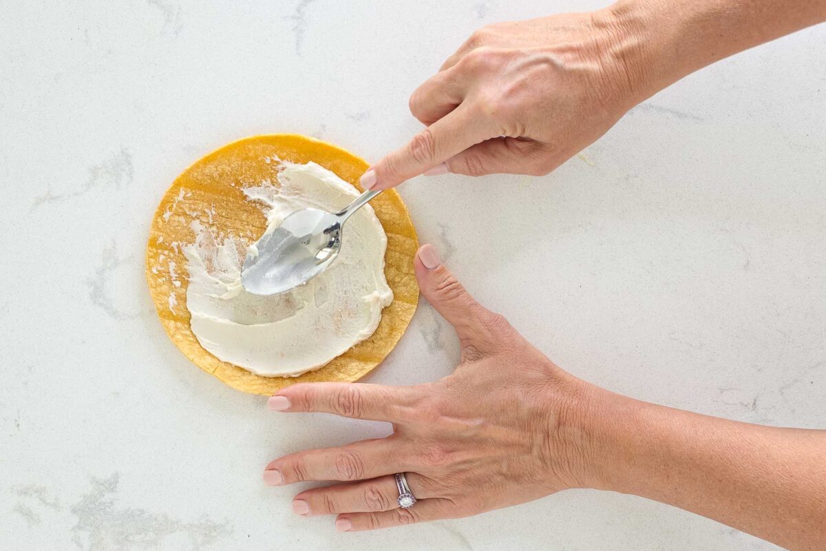 spreading cheese on a tortilla with a spoon