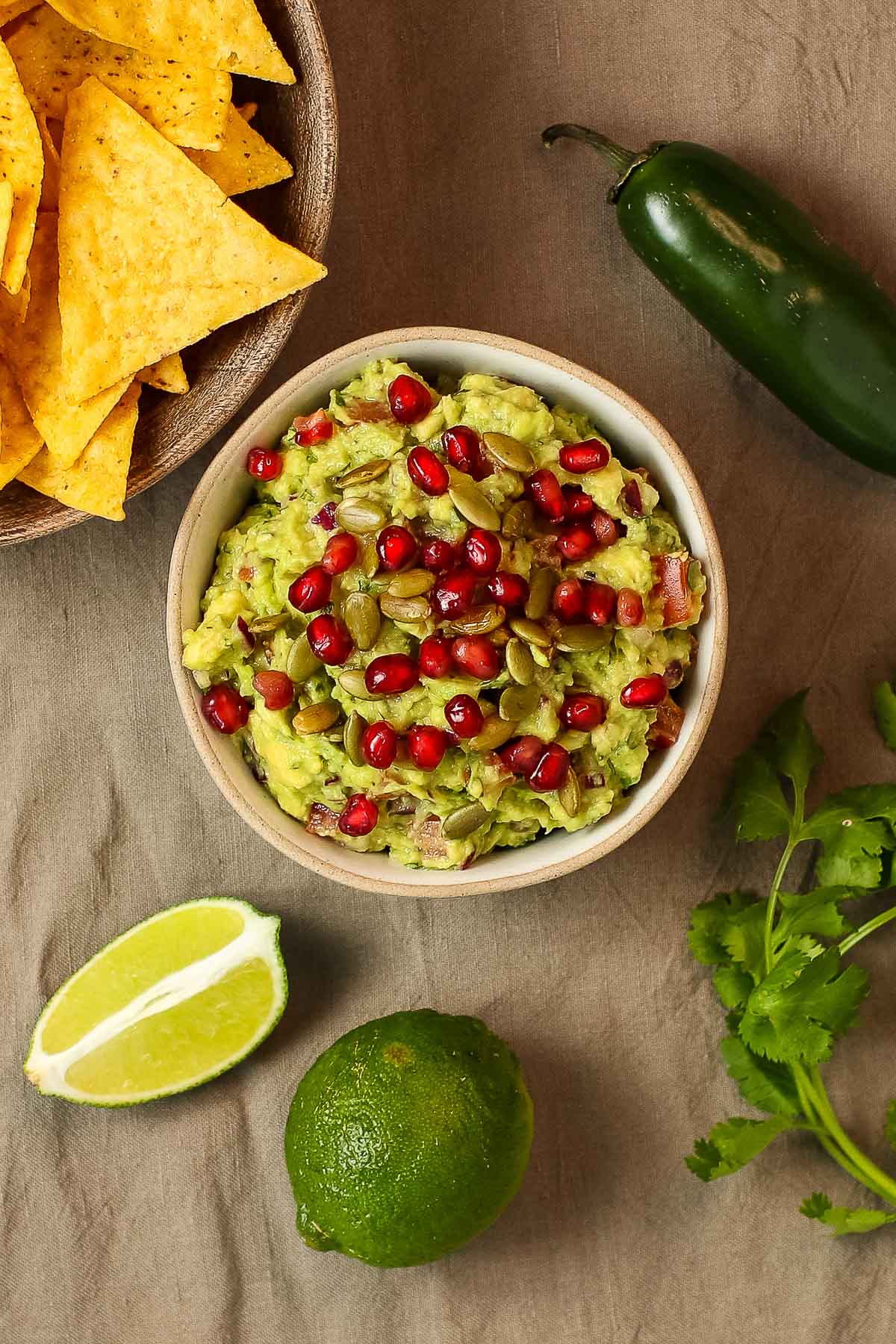 vegan guacamole with chips, pepper and lime on brown towel.