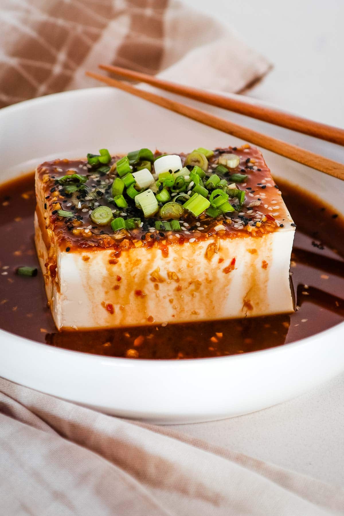 Silken tofu with soy sauce dressing, scallion garnish and chopsticks.
