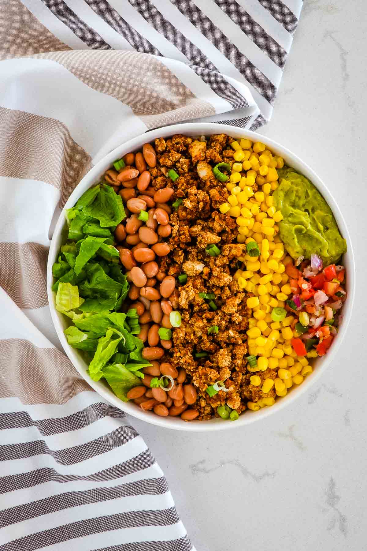 Sofritas bowl with romaine lettuce, pinto beans, corn, pico de gallo, guacamole, garnished with green onion.