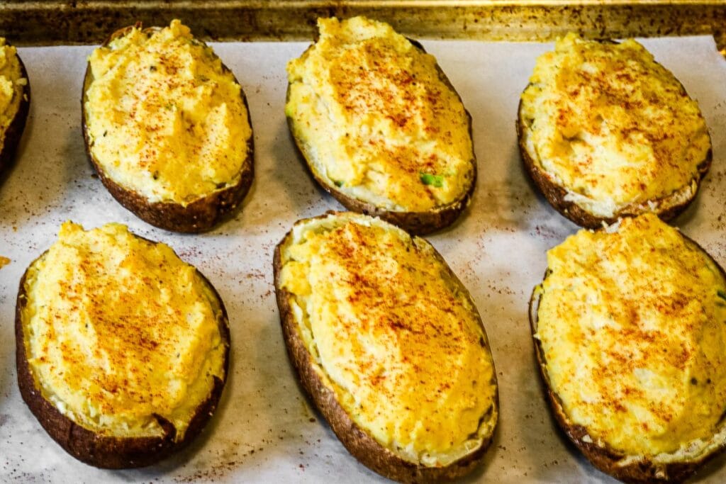 Filled potato shells on a parchment paper lined sheet pan.