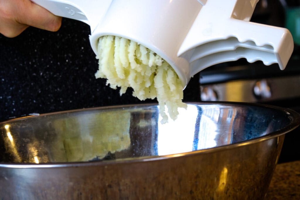 Ricing potatoes into a metal mixing bowl. 