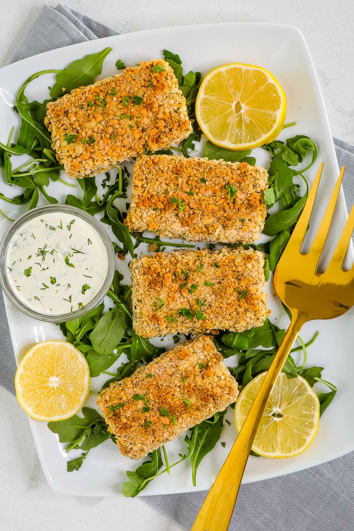 Baked tofu chicken breasts on a platter with arugula, lemon and a dish of ranch dressing. 