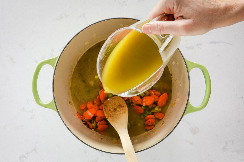 Pouring broth out of a mixing cup into the pot of veggies. 