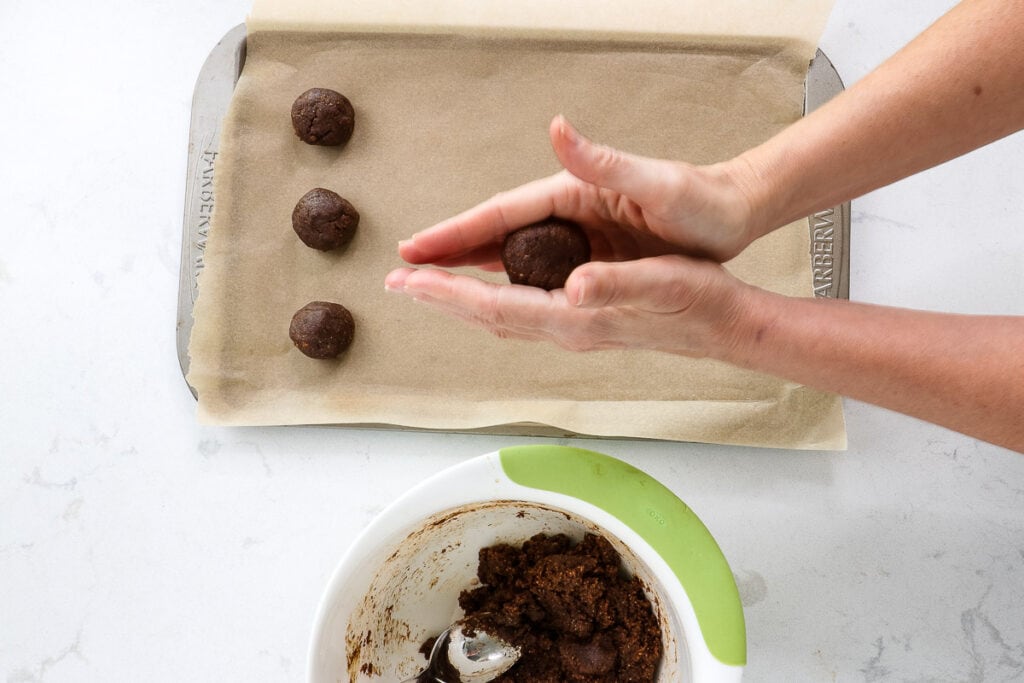 Rolling a ball of dough in my hands, over a baking sheet with parchment paper and finished balls. 