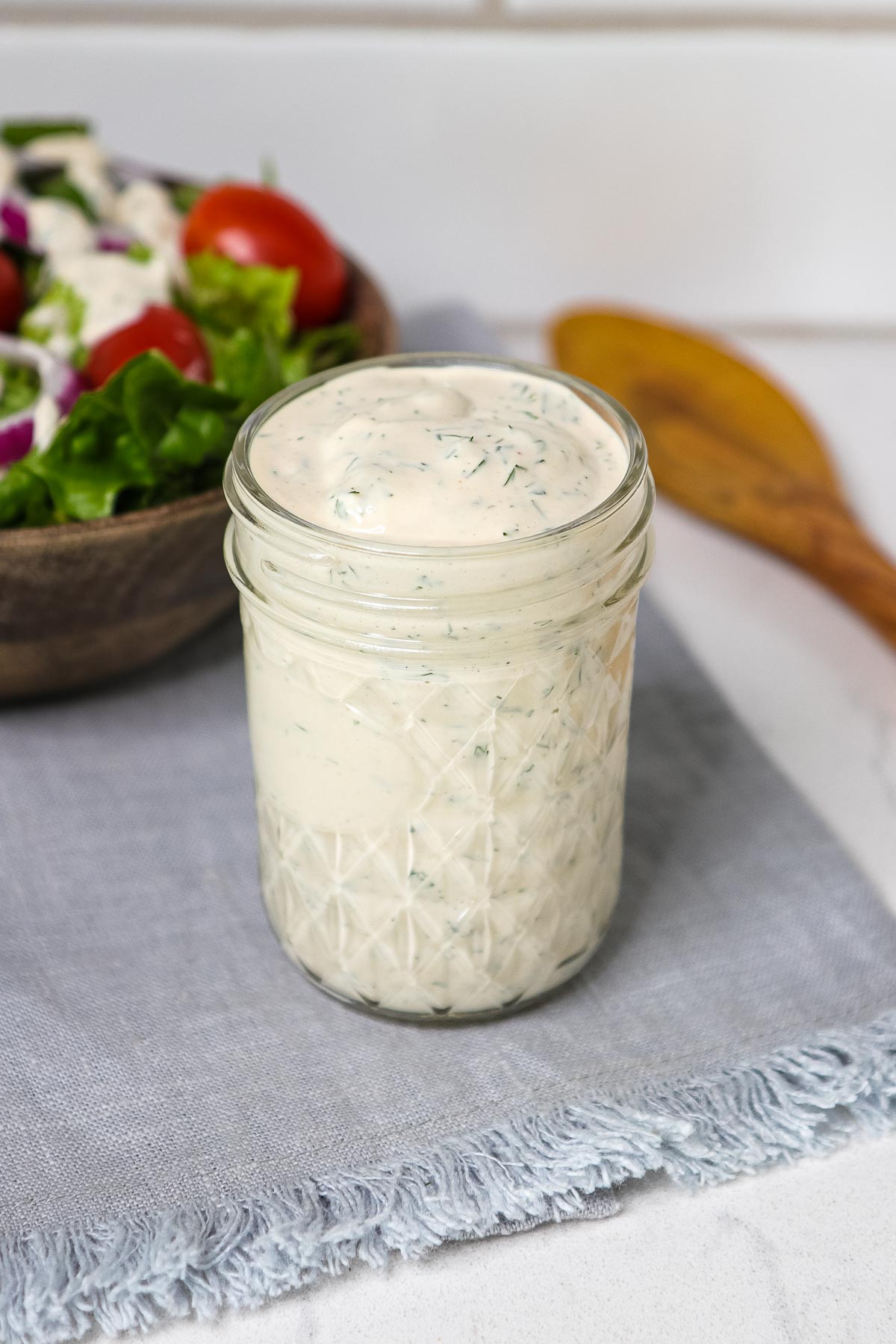 Close up of dressing in a mason jar, with salad and wood spoon. 
