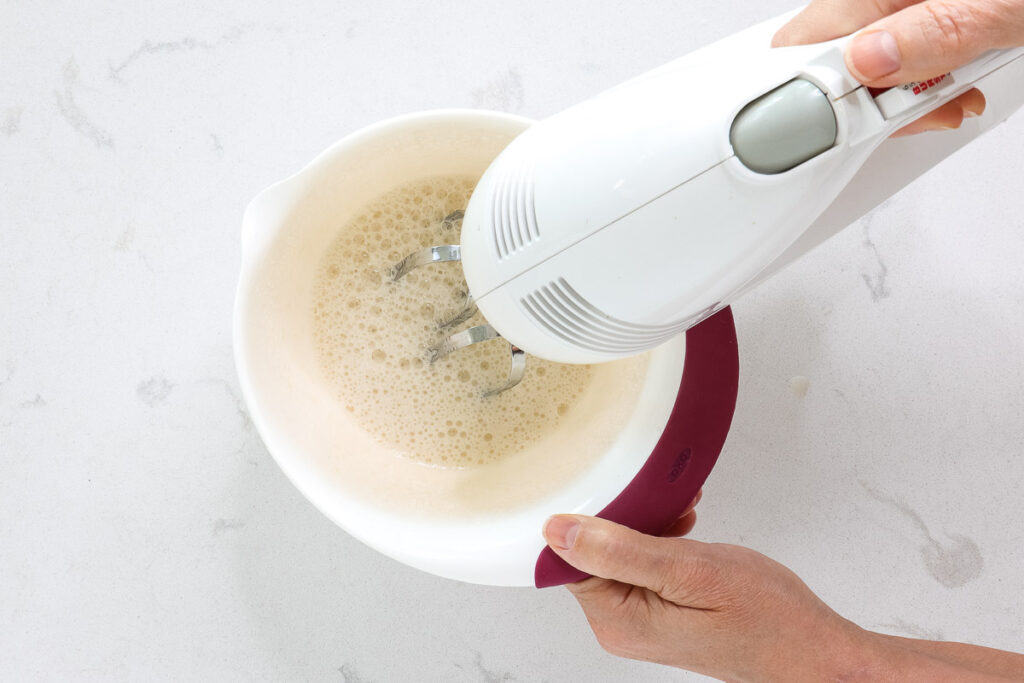 Hand mixer beating frothy white liquid. 