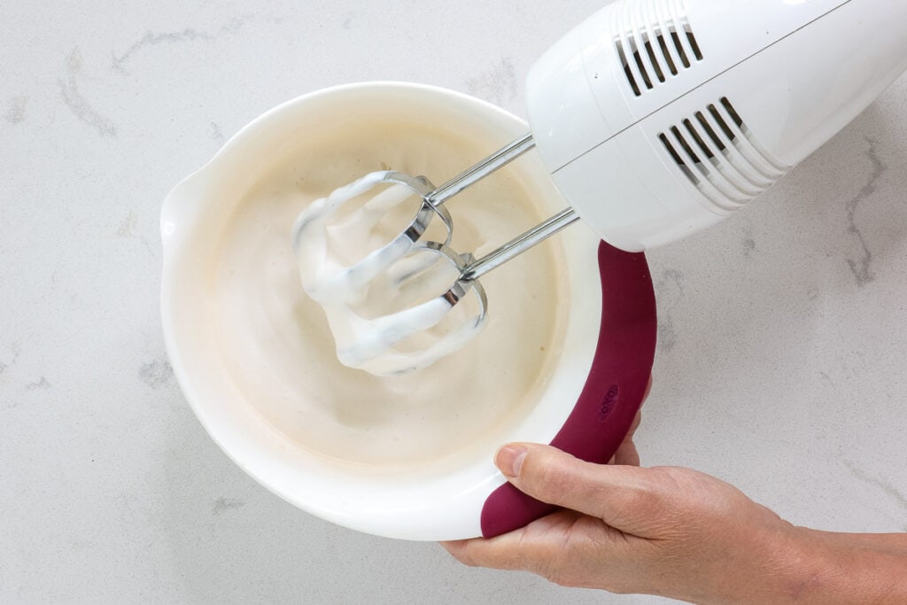 Hand mixer beating thickening white liquid. 