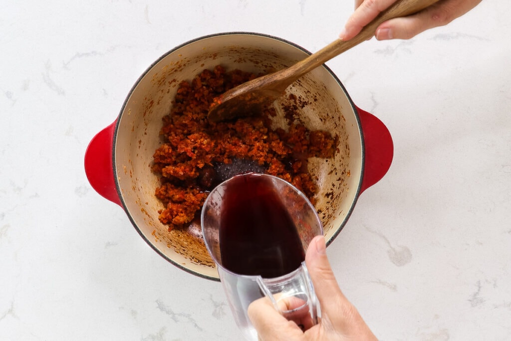pouring red wine into the pot of veggies. 